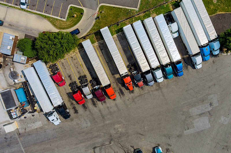 Resting place with various types of trucks in a crowded parking lot off near highway.